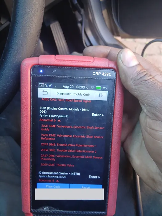 A diagnostic scanner showing engine fault codes, held inside a car